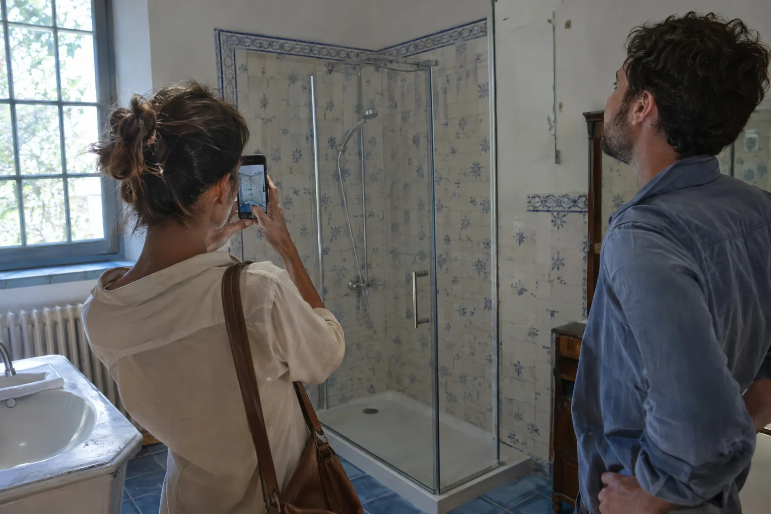 Un couple photographie sa salle de bain avec un téléphone pour demander un devis