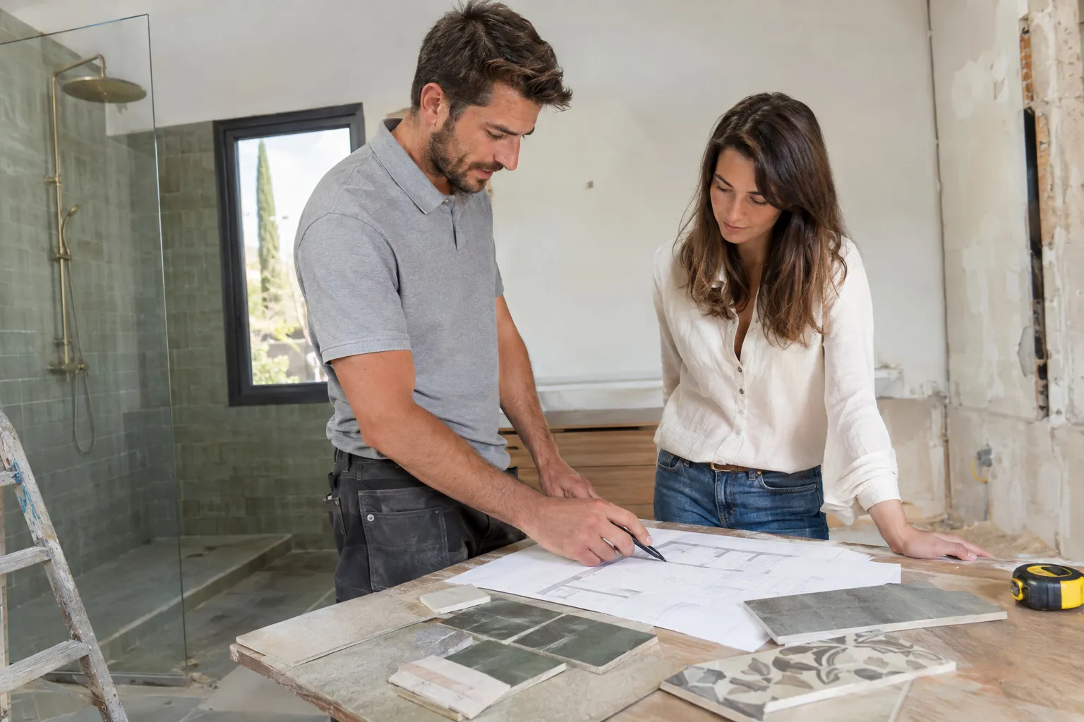 Plan de travail avec échantillons de carrelage, mètre ruban et plan de salle de bain pour estimer le budget d’une rénovation.