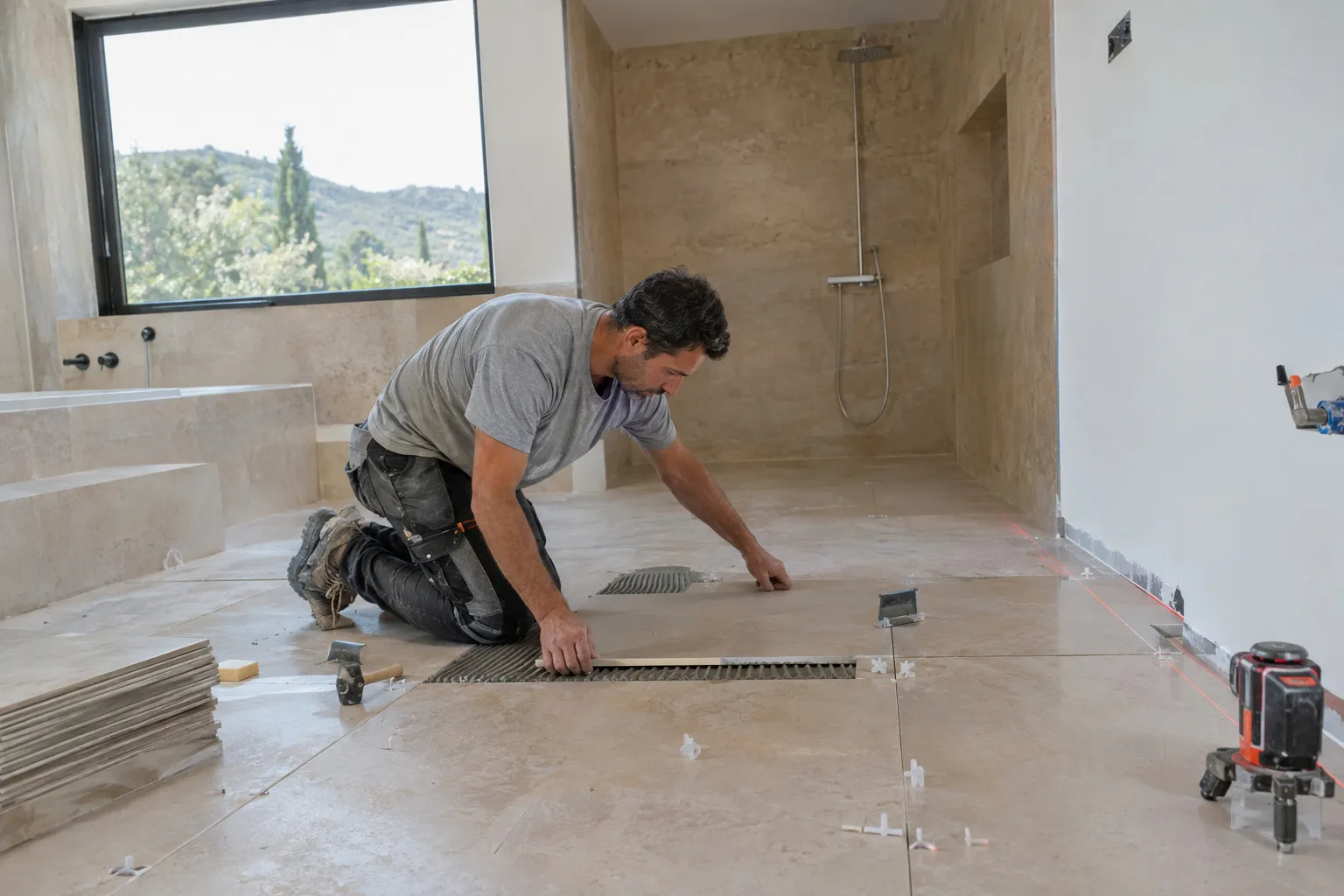 Carreleur posant un carrelage grand format au sol d’une salle de bain, croisillons et niveau laser